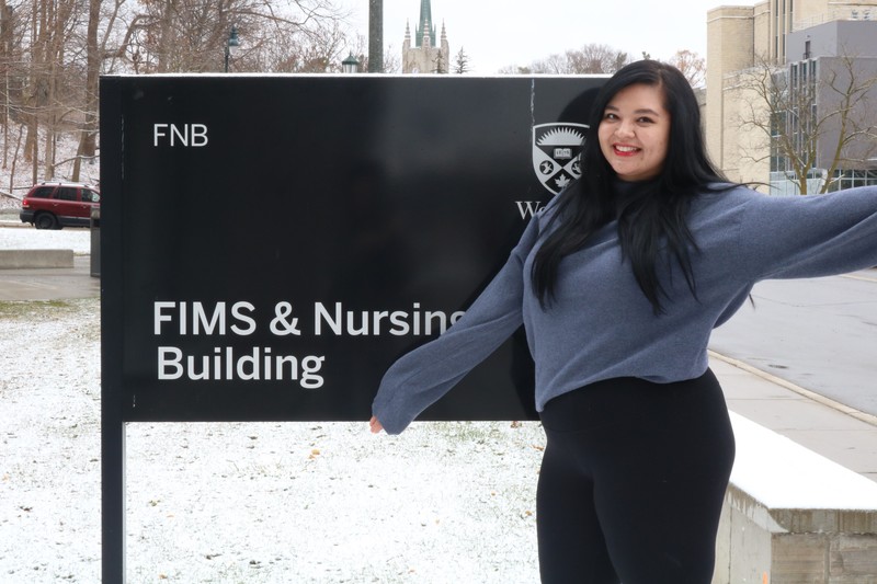 Image of a nursing student posing in front of the sign for the FIMS and Nursing Building.